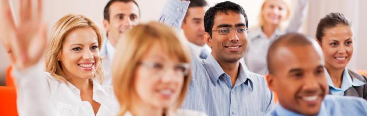 Frequently Asked Questions image - business people sitting in room with hands raised to ask questions